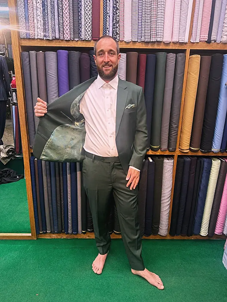 Client in a sage bespoke suit at the fabric wall