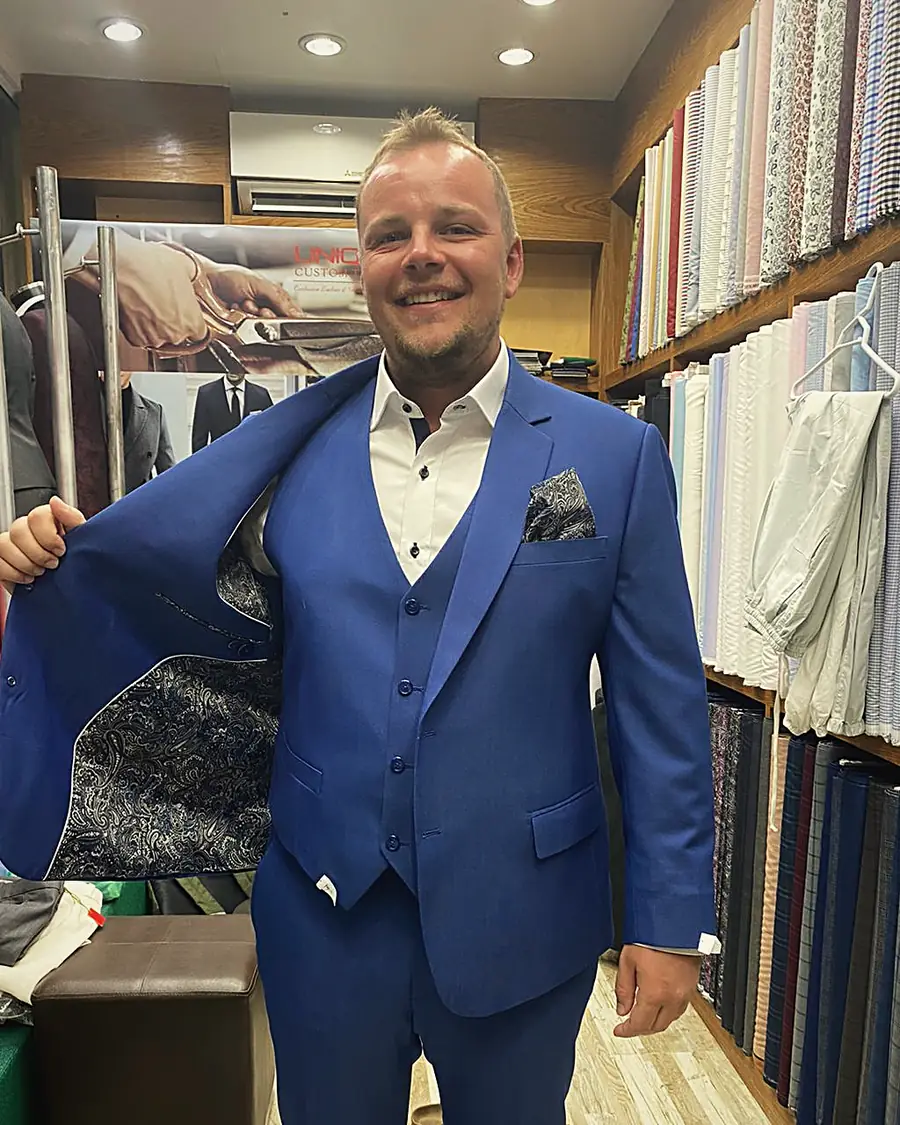 A client showing the paisley lining of his blue three-piece suit in the Unique Custom Tailor shop