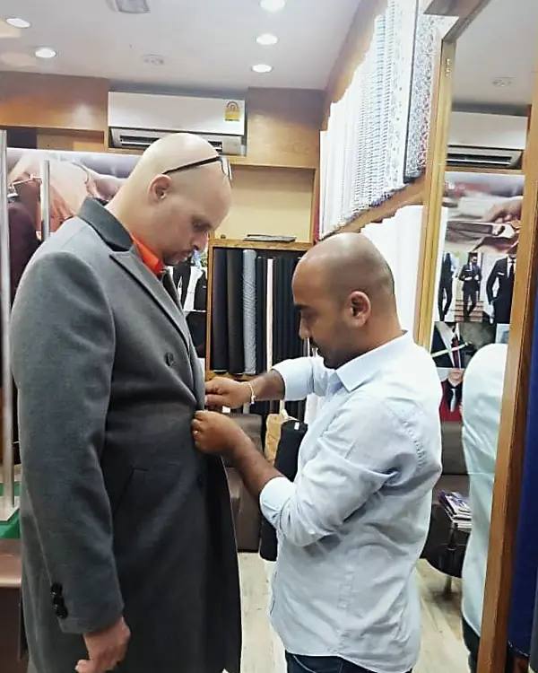 A tailor fitting a grey overcoat on a client in the shop
