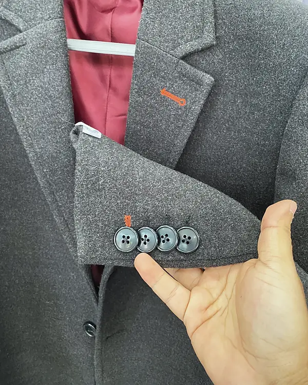 The cuff of a grey jacket with four buttons and a contrast buttonhole