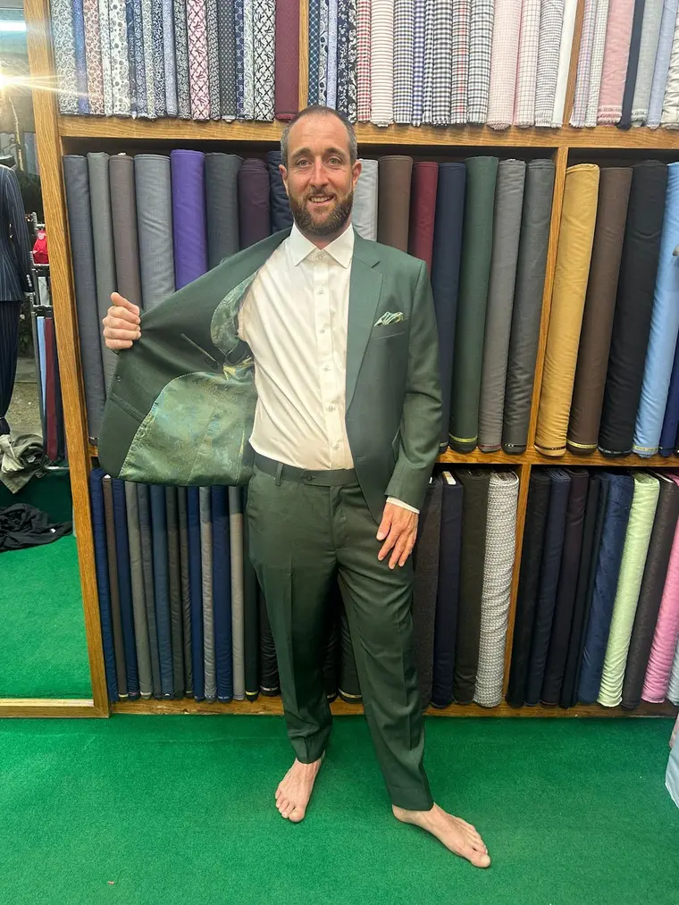 Client in a sage bespoke suit at the fabric wall