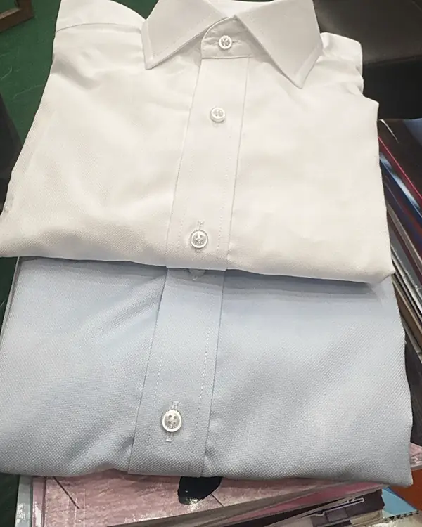 A white and a pale blue made-to-measure shirt, folded, in the shop