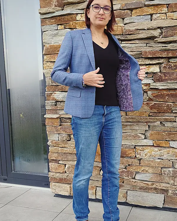 A woman in a tailored blue check jacket against a stone wall